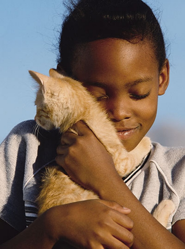 A young african american girl snuggles with a kitty and a smile